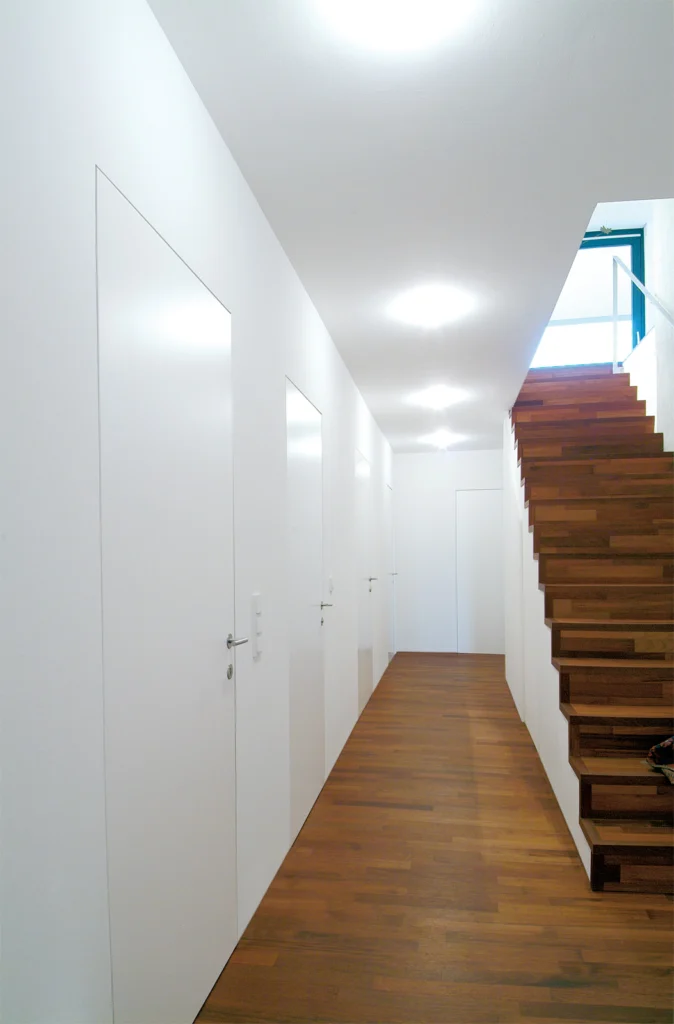 Zargenlose Türen im minimalistischen Flur mit Holztreppe